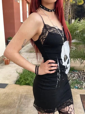 Side-angled outdoor view of a model in the black skull mini dress, showing the slender straps and lace neckline above the pale skull print.