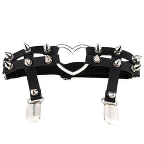 Black double-band thigh garter with cone spikes, an open silver-tone heart ring and two hanging stocking clips, shown against white.