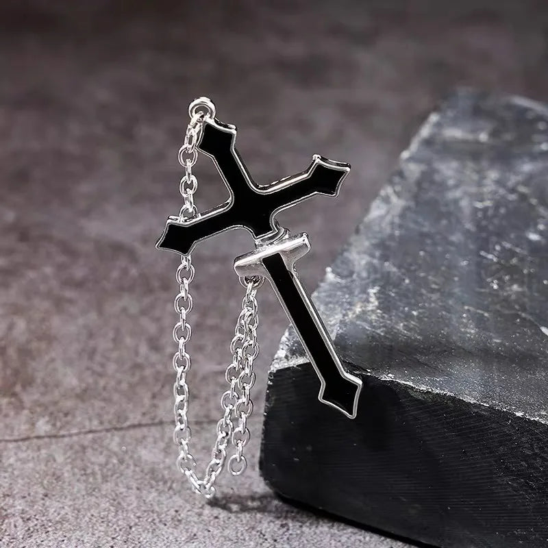 Single black split cross chain earring arranged on a dark textured surface, showing its angular outline, silver-tone edges and hanging chain.