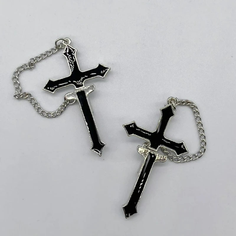 Two black split cross chain earrings laid on a pale surface, with silver-tone outlines and the connected upper and lower pieces visible.
