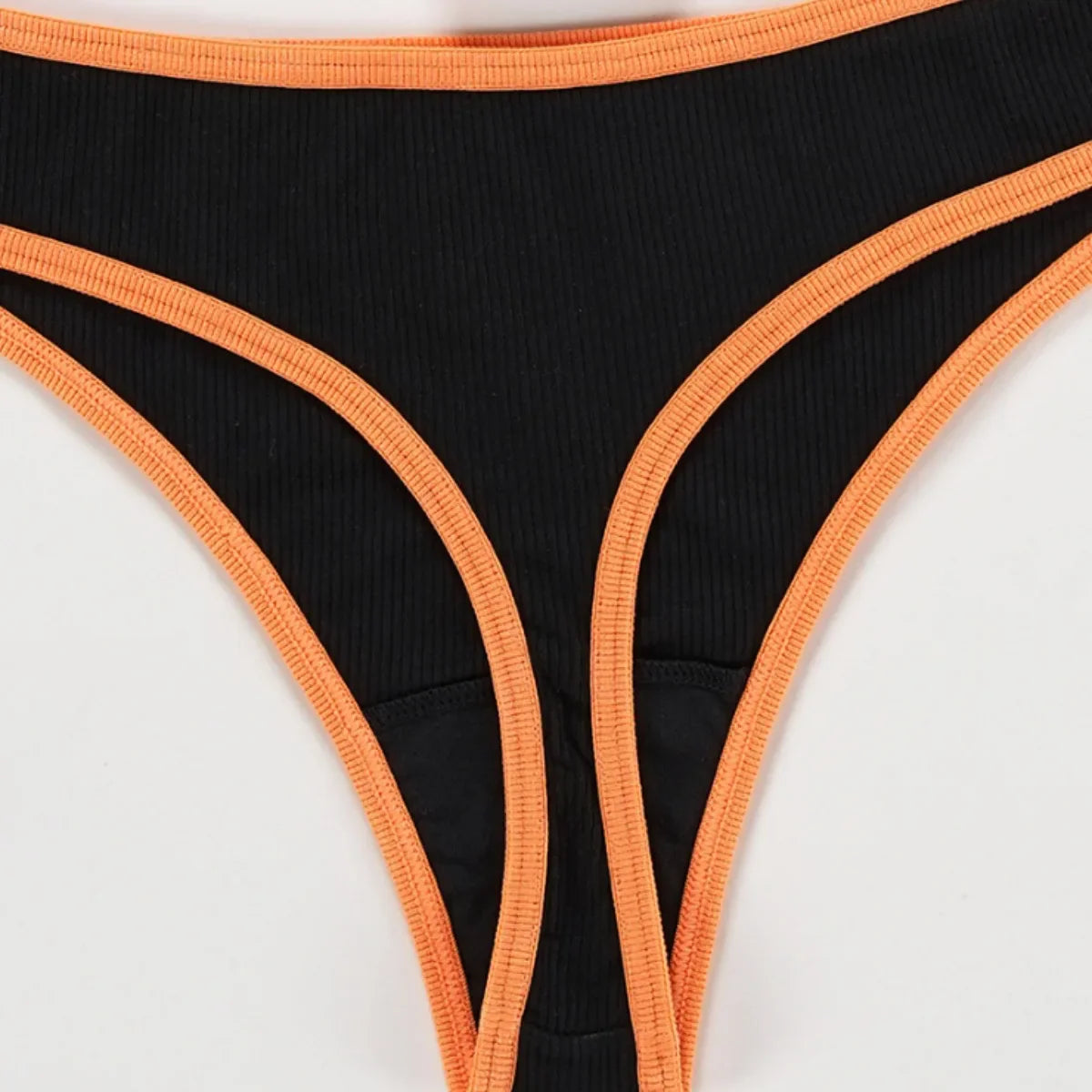 Close view of the back of a black ribbed thong with bright orange edging around the waist and narrow lower section.