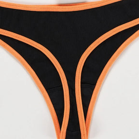 Close view of the back of a black ribbed thong with bright orange edging around the waist and narrow lower section.