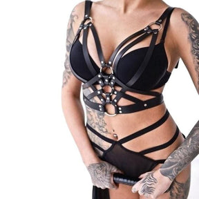 Black triple O-ring chest harness shown from the front over a separate bra and strappy briefs, with angled bands framing the chest and upper waist.