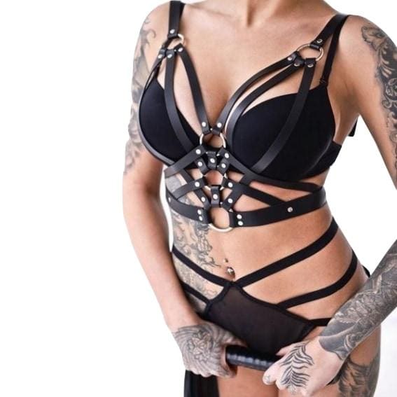 Black triple O-ring chest harness shown from the front over a separate bra and strappy briefs, with angled bands framing the chest and upper waist.