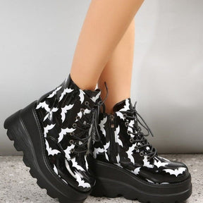 Angled upper view of black platform boots with white bats, showing the laced fronts, rounded toes and silver-tone eyelets.