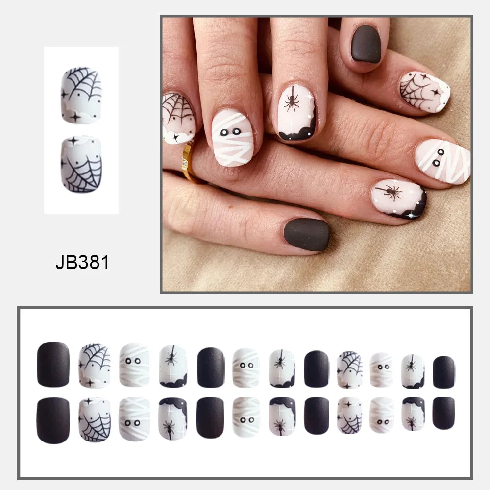 Short black-and-white mummy nail design with wrapped eyes, spiders and webs, pictured worn above a layout of nail tips.