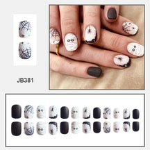 Short black-and-white mummy nail design with wrapped eyes, spiders and webs, pictured worn above a layout of nail tips.