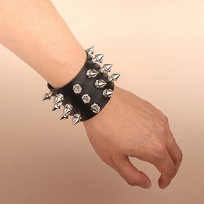 Wide black cuff bracelet worn on a wrist, showing silver-tone pointed spikes along the outer rows and faceted studs across the centre.