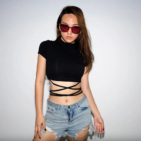 Angled studio outfit view of the black crop top and denim shorts, showing the crisscrossed waist ties and short sleeves.