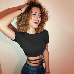 Smiling model with curly hair wearing the black crop top and jeans, showing the wrapped waist ties beneath the short hem.