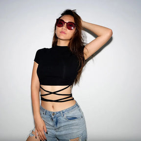 Model with one arm raised wearing the black wrap top and denim shorts, showing the high neckline and crossed waist ties.