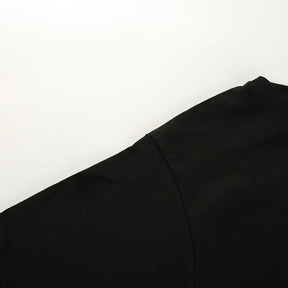 Close-up of the black top's shoulder and sleeve seam against a white surface.