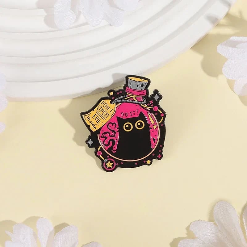 Witchy black cat bottle brooch on a pale yellow surface with white flowers, showing pink enamel and star details.