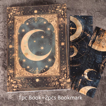 Dark celestial moon journal with an ornate gold-coloured crescent cover and two matching bookmarks, arranged on textured fabric.