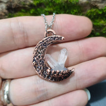 A copper-toned crescent quartz moon pendant necklace with textured finish holding clear quartz crystals