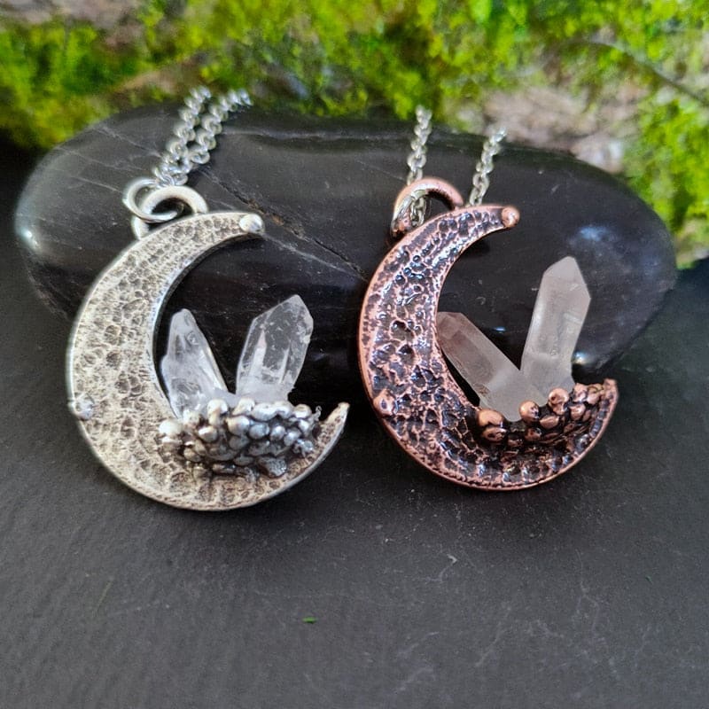Two crescent quartz moon pendant necklaces in silver and copper with clear quartz crystals in textured metal bases