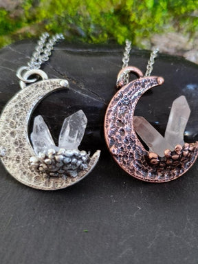 Two crescent quartz moon pendant necklaces in silver and copper tones with clear quartz crystals and hammered texture