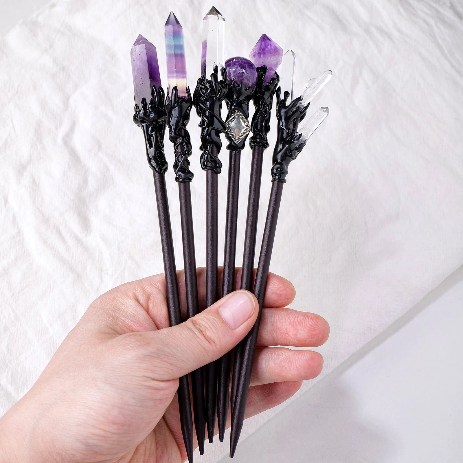 A hand holding several gothic crystal hair sticks to show their scale and toppers