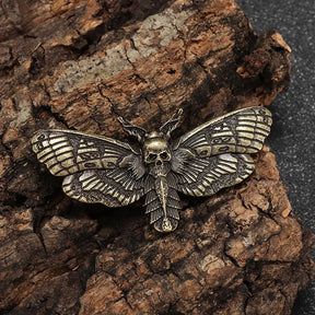 Gold-tone death head moth pin on bark, showing its sculpted skull, segmented body and patterned wings.