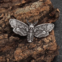 Antique silver tone moth brooch on rough bark, with a small skull at the centre and dark patterned wing recesses.