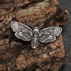 Antique silver tone moth brooch on rough bark, with a small skull at the centre and dark patterned wing recesses.