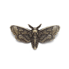 Gold-tone gothic moth brooch isolated against white, with a raised skull and engraved-looking wing details.