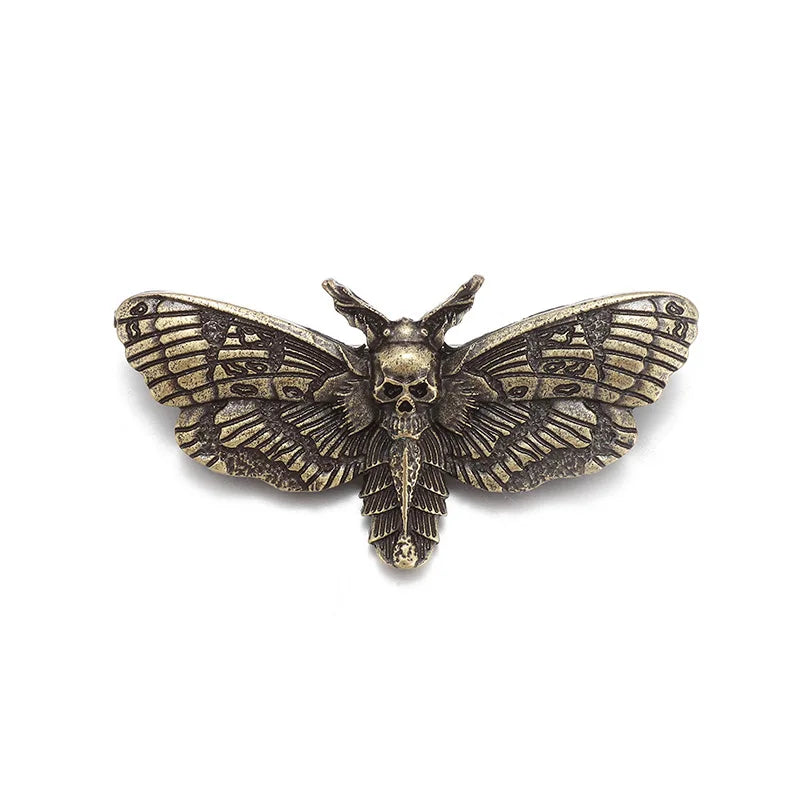 Gold-tone gothic moth brooch isolated against white, with a raised skull and engraved-looking wing details.