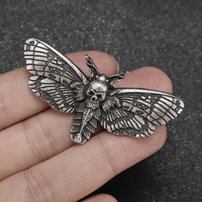 Antique silver-tone moth brooch resting across fingers, showing its raised skull centre and finely patterned wings.