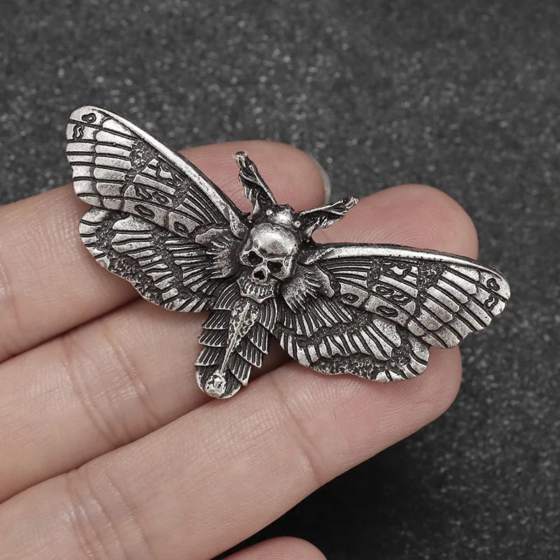 Antique silver-tone moth brooch resting across fingers, showing its raised skull centre and finely patterned wings.