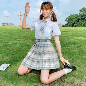 A school girl wearing an electric plaid skirt in beige gray white with color options paired with a blue shirt and tie