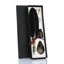 Black feather calligraphy gift set in an open box, with a red ribbon, spare nibs, bottle and ornate pen stand.