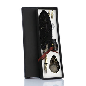 Black feather calligraphy gift set in an open box, with a red ribbon, spare nibs, bottle and ornate pen stand.