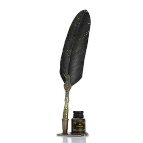 Black feather dip pen with an ornate antique-tone handle standing beside a bottle against white.
