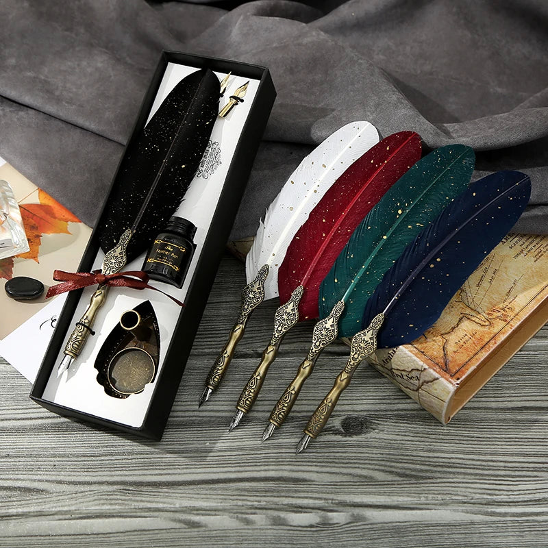 Black feather quill gift box beside loose white, red, green and blue feather pens on a writing table, showing the available colours.