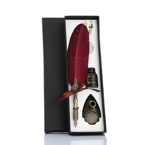 Red feather quill gift set in a fitted black box with spare nibs, a bottle and shield-shaped stand.