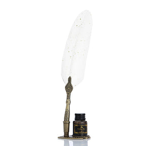 White feather quill with gold-coloured speckles and an ornate handle, standing beside its bottle.