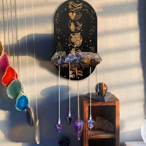 Floral Spheres wall shelf holding a row of stones, with necklaces suspended below the ledge in warm sunlight.