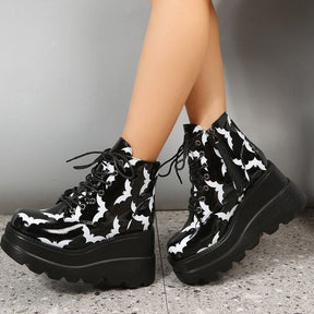 Black-and-white bat platform boots worn with crossed feet, bringing the printed toe shapes and thick soles into the foreground.