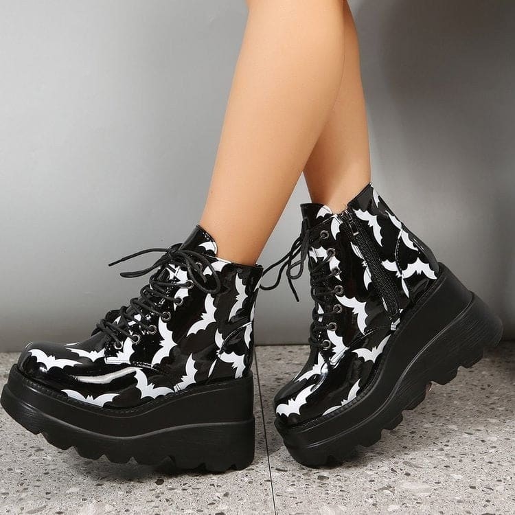 Black-and-white bat platform boots worn with crossed feet, bringing the printed toe shapes and thick soles into the foreground.
