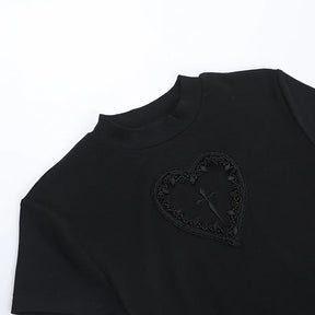 Angled close-up of the black T-shirt neckline and lace-bordered heart detail on a white surface.