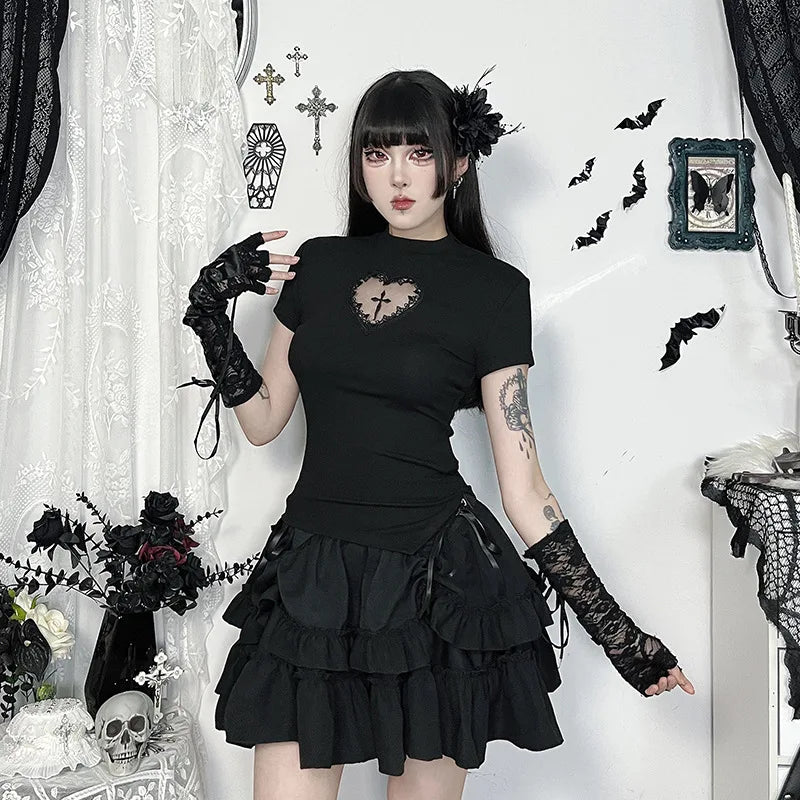 Black heart-cutout T-shirt styled with a short tiered skirt and lace arm warmers in a room with bat and cross decorations.