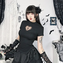 Black gothic T-shirt with a lace-edged heart cutout and central cross, worn with a ruffled black skirt. A seated pose against white lace curtains shows the short sleeves and shaped hem.
