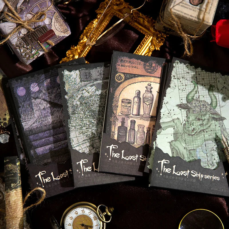 Four witchy stationery paper packs in purple, green, grey and amber tones, arranged beside ornate frames and a pocket watch.