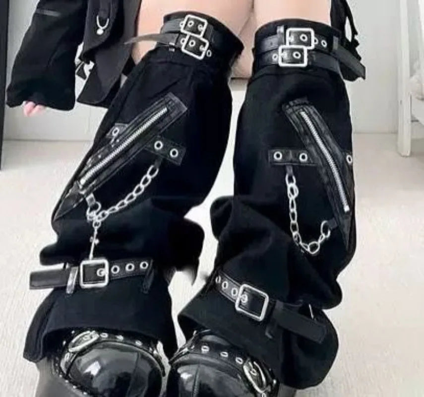 Detail of black punk leg warmers showing eyelet straps, square buckles, diagonal zippers and hanging cross detail.