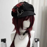 Red plaid gothic newsboy cap on a mannequin, showing its curved brim, decorative chains and dangling cross charm.