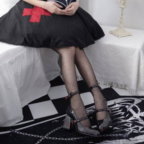 Paired gothic Mary Janes beneath a black skirt with a red cross, with dotted tights highlighting the slim ankle and instep straps.