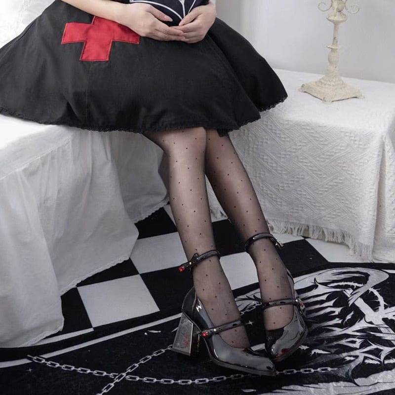Paired gothic Mary Janes beneath a black skirt with a red cross, with dotted tights highlighting the slim ankle and instep straps.