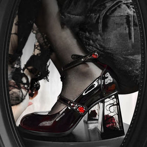 Side detail of a dark wine-red Mary Jane showing the ankle strap, instep strap and red jewel-like accents above a clear rose-filled block heel.