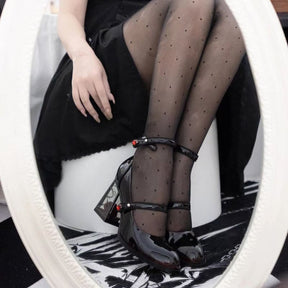Seated view of the rounded dark red toes and double straps on rose-heel Mary Janes, with one clear heel visible beside an ornate mirror.