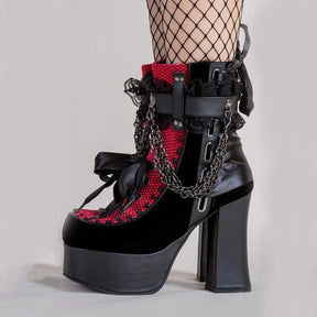 Outer side of a red platform ankle boot worn with fishnet tights, showing draped chains and black lace trim.